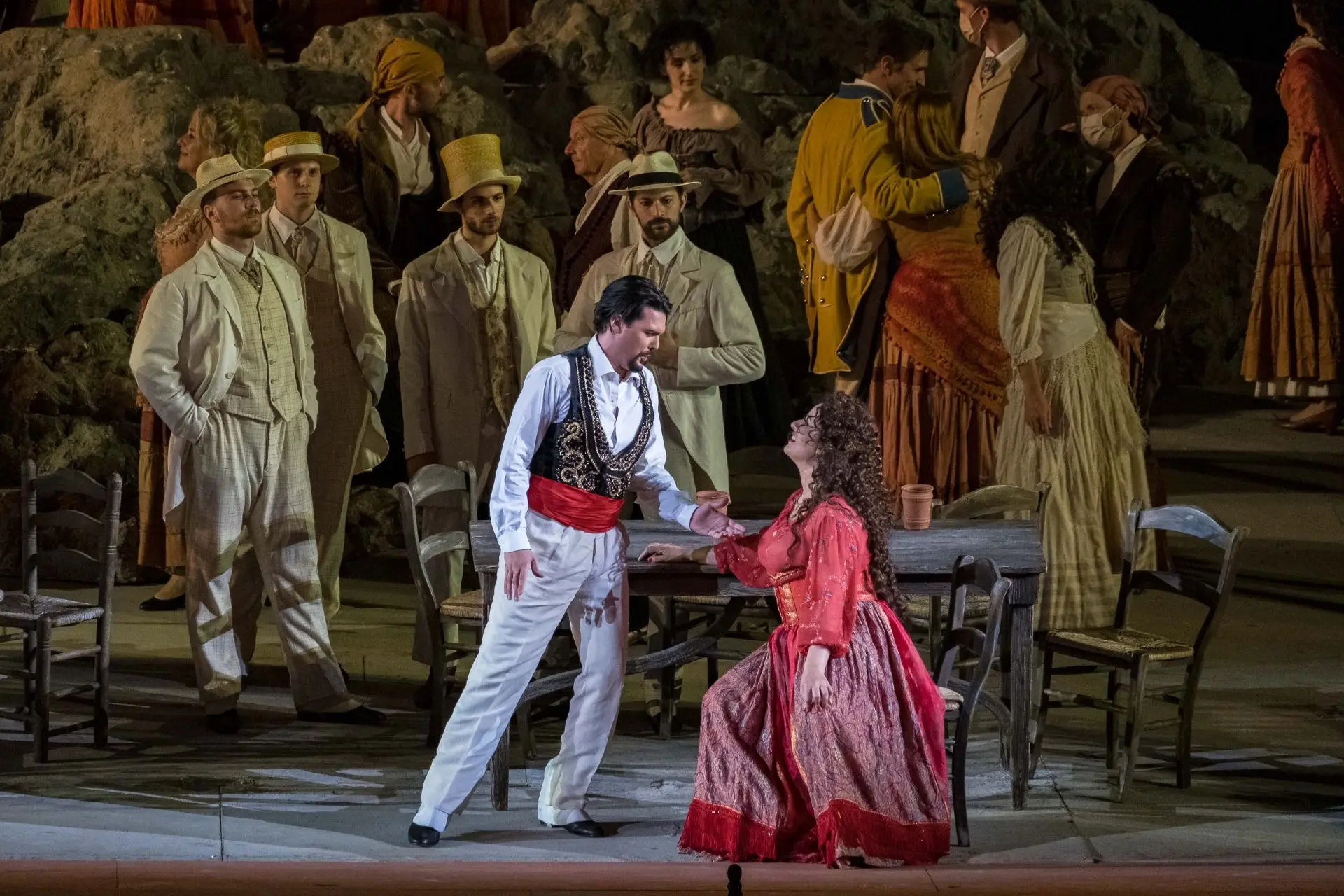 Escamillo e Carmen sono al centro della scena. Carmen è seduta a uno dei tavoli di legno della taverna di Lillas Pastia, mentre Escamillo è in piedi, di fronte a lei. I due si guardano intensamente. Escamillo indossa una camicia bianca di cotone con sopra un gilet nero, molto scollato, con decorazioni dorate; dei pantaloni bianchi di cotone e una fascia rossa in vita. Ai piedi, delle scarpe stringate nere, lucide. Ha i capelli castani, corti, e il pizzetto. Carmen indossa un abito composto da un corpetto di colore rosso, semitrasparente, a maniche lunghe decorate con dei piccoli fiori colorati, una gonna ampia, lunga fino alle caviglie, composta da stoffe di tessuti diversi, sulle tonalità del rosso e del viola. In vita indossa un’ampia fascia rigida, che le stringe il busto all’altezza del seno. Ha i capelli ricci, castani, lunghi fino a circa metà schiena.